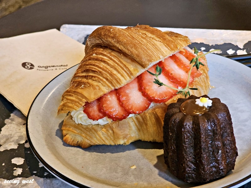 Ongeundal Café 的草莓可頌夾忌廉甜點，旁邊配上可麗露，擺盤精緻，背景為店家紙巾與金屬桌面。